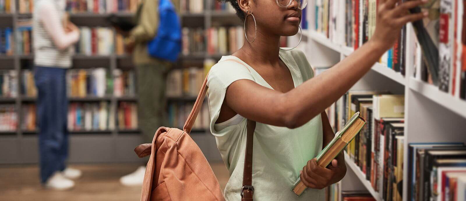 Image of a adolescent pulling a book off a shelf at a school library. Representing the stress that therapy for teens can help with in Reading & Wyomissing, PA. You can find teen counseling "near me" with an online teen therapist in Pennsylvania.
