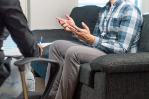 Image of a man sitting on a grey couch talking to an anxiety therapy in Reading, PA. Showing what anxiety treatment for anxiety symptoms looks like in Pennsylvania.