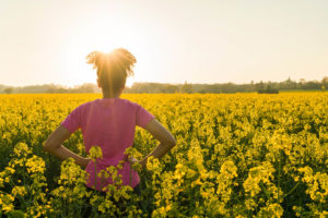 Image of a woman standing in a filed of yellow flowers as the sun shines brightly. Representing what it can feel like after addressing anxiety symptoms in therapy for anxiety treatment in Reading, PA.