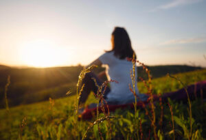 Image of a woman watching the sun while sitting on a grassy hill. Representing the change in negative thoughts from CBT therapy, or cognitive behavioral therapy, in Reading, PA. Get help with CBT for depression.