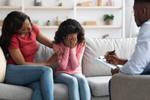 Image of a mom and daughter sitting together on a couch meeting with a family therapist. Showing what family therapy, also known as family counseling, can look like in Wyomissing and Reading, PA.