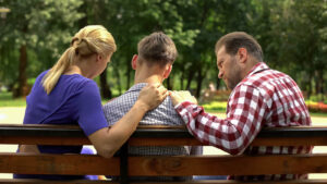 Image of a mom, dad, and son sitting on a bench in a park. Representing loved ones that could benefit from meeting with a family therapist in Reading, PA. During family therapy, or family counseling, loved ones can communicate openly and honestly.