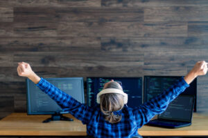 Image of a woman sitting in front of 3 computer monitors with her arms raised. Showing that positive outcome of going to therapy for work anxiety in Reading and Wyomissing, PA.