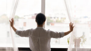 Image of a woman in Wyomissing, PA standing at a window. Representing work-life balance which is something that would be suggested in counseling for anxiety by an anxiety therapist. Get additional suggestions for addressing work anxiety.